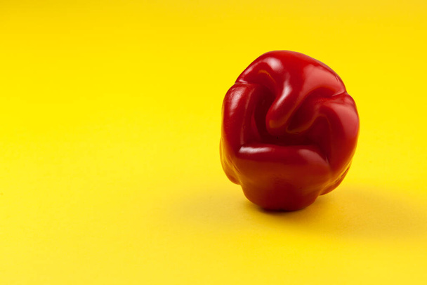Ugly red bell pepper on yellow background with copy space. Concept - reduction of food organic waste. A deformed crooked vegetable looks like a grimace of a fairytale character. - Fotó, kép