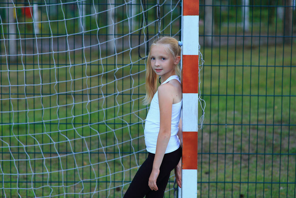 Een meisje poseren in de buurt van een voetbaldoel op een sportveld. - Foto, afbeelding