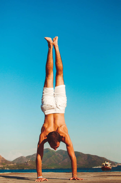 Strong healthy handsome athletic man doing morning work-out, practicing yoga on the seaside, standing on hand upside down. Relaxe and meditation, wellbeing and healthy lifestyle concept - Fotoğraf, Görsel