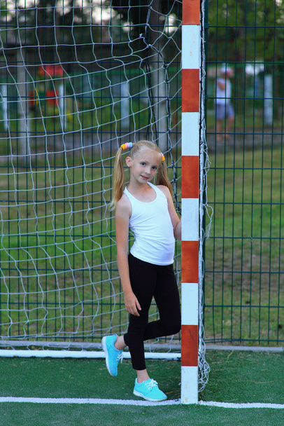Una chica posando cerca de un gol de fútbol en un campo de deportes. - Foto, Imagen