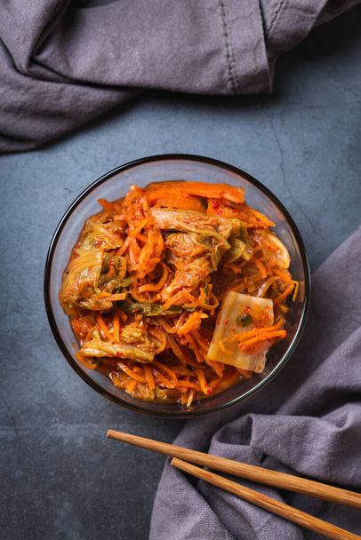 Σπιτική παραδοσιακή Κορεάτικη σαλάτα λάχανο kimchi με chopsticks σε σκούρο τραπέζι. Ζυμωμένο χορτοφαγικό, vegan διατηρημένο έντερο υγιεινής διατροφής έννοια. Επίπεδη lay, αντίγραφο φόντο χώρο. - Φωτογραφία, εικόνα