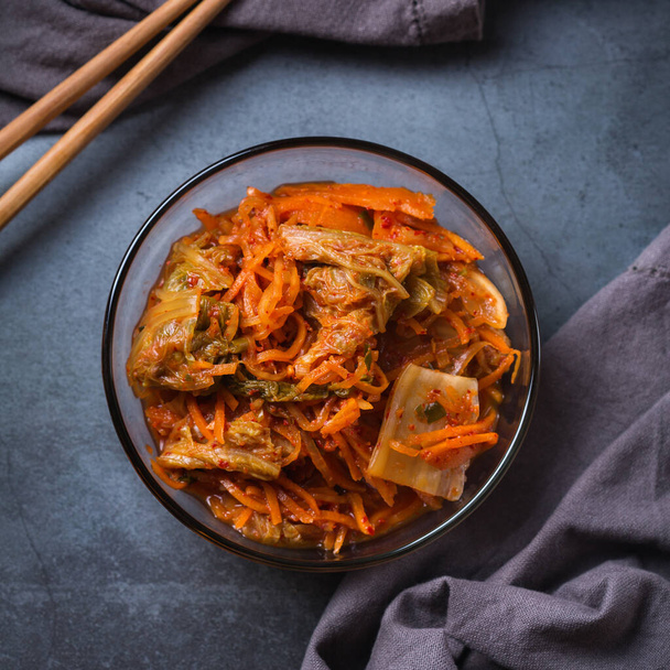 Hausgemachter traditioneller koreanischer Kimchi-Krautsalat mit Stäbchen auf einem dunklen Tisch. Fermentiertes vegetarisches, vegan konserviertes Darmgesundheitskonzept. Flache Lage, Kopierraum Hintergrund. - Foto, Bild