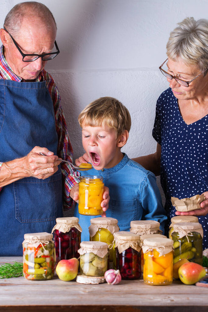 幸せな高齢者、祖母、祖父と若い男の子、孫の自家製フルーツコンポートの試飲。保存され、発酵,漬物やマリネ食品の概念.収穫保存、家族時間 - 写真・画像