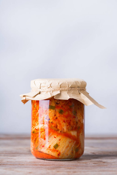Homemade organic traditional korean kimchi cabbage salad in a glass jar on a wooden table. Fermented vegetarian, vegan preserved gut health food concept - Fotoğraf, Görsel