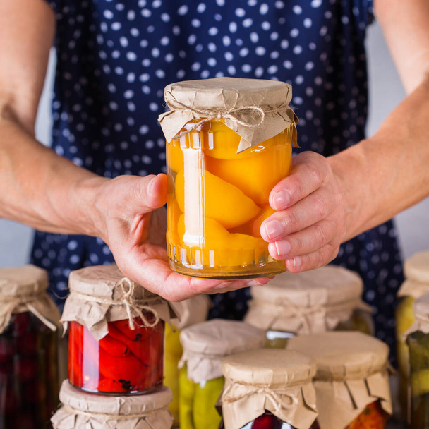 Senior mature woman holding in hands jar with homemade preserved and fermented food. Variety of pickled and marinated vegetables, fruit compote. Housekeeping, home economics, harvest preservation   - Fotoğraf, Görsel