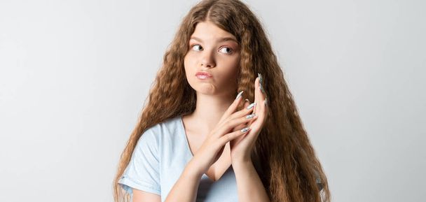 Foto de la joven europea reflexiva con pelo largo rizado se ve con expresión de ensueño a un lado. Aislado sobre fondo blanco. - Foto, Imagen