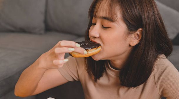 Comer donut quando tomar e entregar. A comida rápida leva-nos para casa. Estilo de vida da mulher asiática na sala de estar. Distanciamento social e nova normalidade. - Foto, Imagem