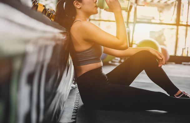 Asian woman exercise and lifestyle at fitness gym. Sporty woman drinking water after workout and training. Wellness and healthy for bodybuilding. - 写真・画像