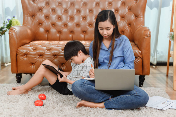 Madre asiatica lavora a casa. Mamma insieme al figlio. Educazione online per bambini. Nuovo stile di vita normale e attività familiare. - Foto, immagini