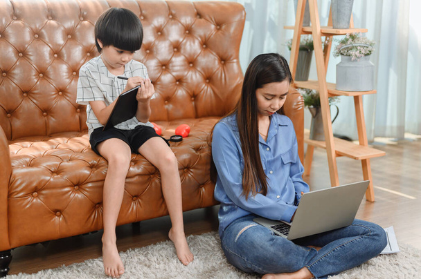 Asiatische Mütter arbeiten zu Hause. Mutter mit Sohn. Online-Bildung für Kinder. Neuer normaler Lebensstil und familiäre Aktivitäten. - Foto, Bild
