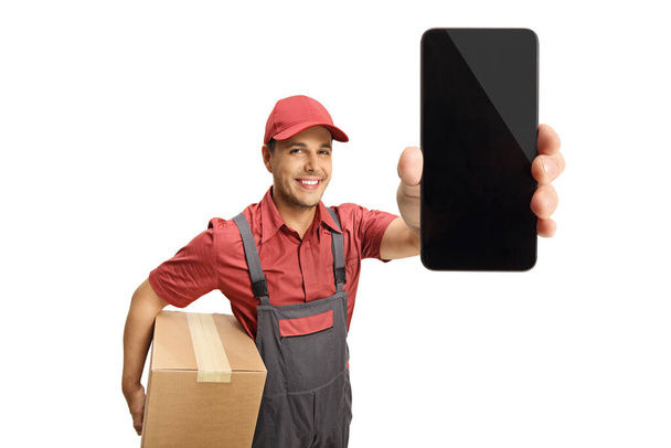 Delivery guy holding a box and a mobile phone isolated on white background  - Fotografie, Obrázek