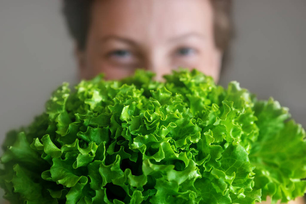 Jonge volwassen mooie blanke vrolijke glimlachende vrouw portret met groene verse sla salade gewas in het gezicht. Gezond voedsel en voeding concept. Groene oraganische eco bio natuurlijke veganistische maaltijd. - Foto, afbeelding