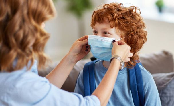 Coronavirus covid-19 ve viral enfeksiyonları önleme kavramı. Anne, okul için evden ayrılmadan önce küçük oğlu için tıbbi maske takıyor. - Fotoğraf, Görsel