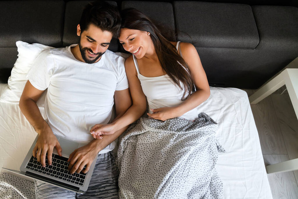 Happy couple with laptop in bed reading news and smiling - Foto, imagen