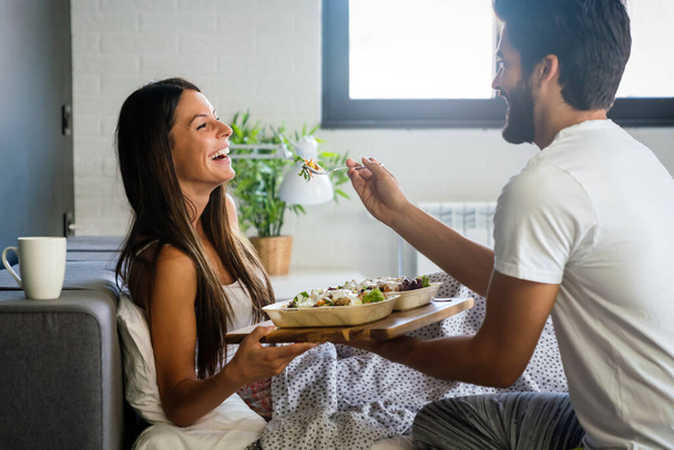 Happy man bringing the breakfast to his beautiful girlfriend on the bed - 写真・画像