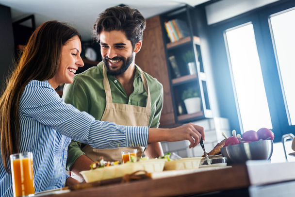 Portrait of happy young couple cooking together in the kitchen at home. - Фото, изображение