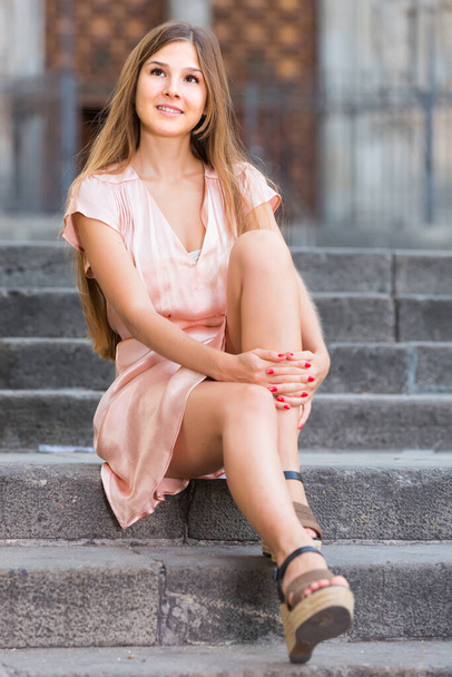 young female in rose dress sitting in city - Foto, imagen