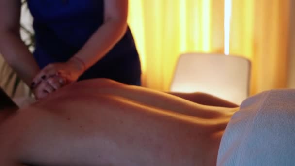 Sesión de masaje en el centro de spa con iluminación cálida - doctora masajeando a sus clientes espalda y cuello con aceite - Metraje, vídeo