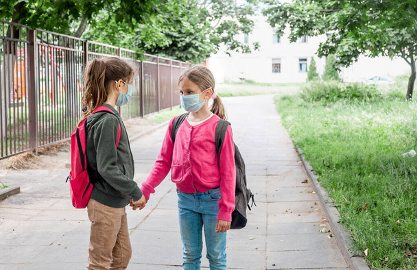 Während der Coronavirus-Pandemie wieder in der Schule. Zwei Schulmädchen tragen Masken und gehen zur Schule. - Foto, Bild