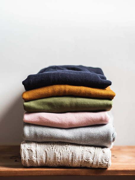 Pile of varicolored autumn clothes on a wooden background, sweaters, knitwear, copy space - Photo, Image