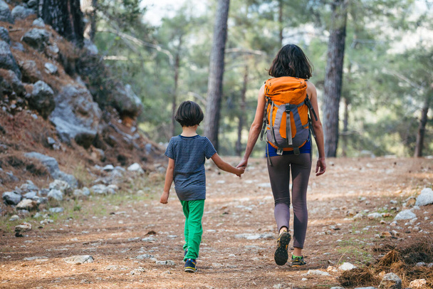 Женщина гуляет с сыном через лес. Мальчик с матерью отправляются в поход. Ребенок с рюкзаком в парке. Путешествуйте с детьми. Ребёнок держит маму за руку. Горная тропа. - Фото, изображение