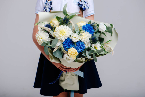 A bouquet of flowers, packed in beige paper in the hands of a girl with pigtails on a light background. Bouquet of hydrangea, dahlia, tulip, eustoma, celosis, eucalyptus - Zdjęcie, obraz