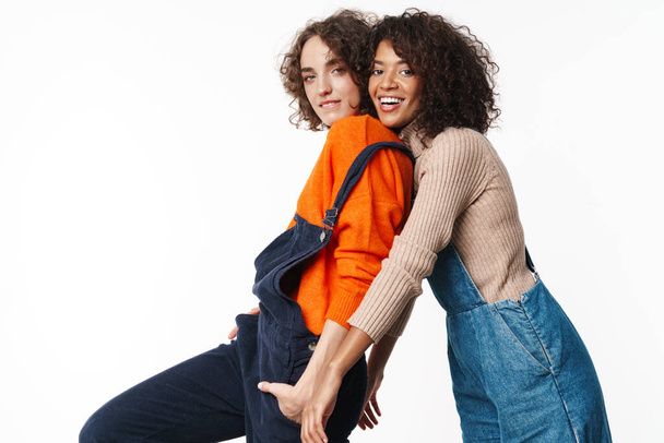 Portrait of joyful multinational women in overalls looking at camera and hugging isolated over white background - Photo, image