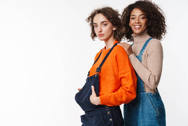 Portrait of lovely multinational women in overalls looking at camera and hugging isolated over white background - Foto, Imagem