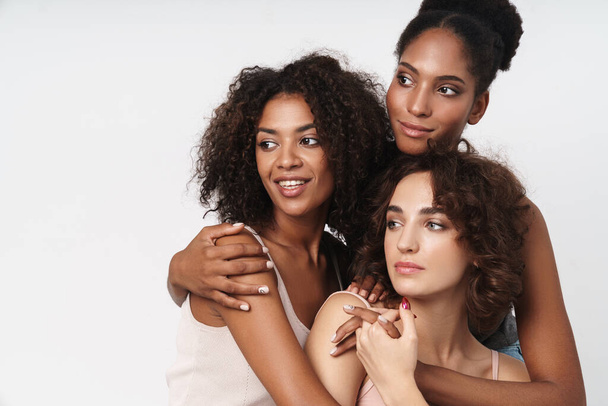 Portrait of three beautiful multiracial women smiling and looking aside isolated over white background - Fotó, kép
