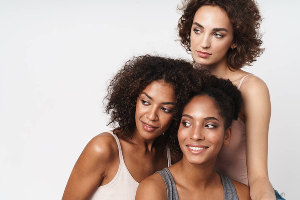 Portrait of three joyful multiracial women smiling and looking aside isolated over white background - Foto, Imagem