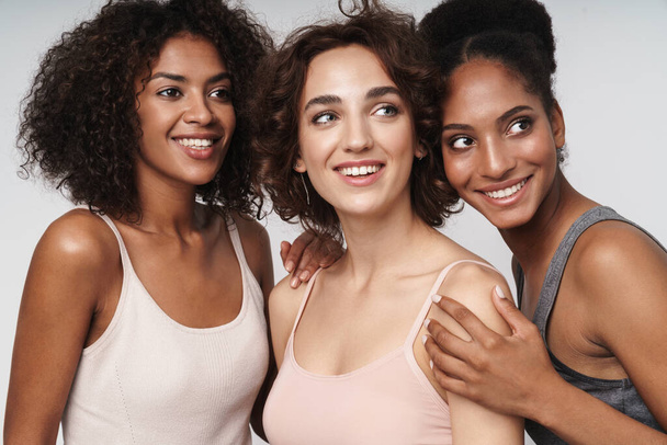 Portrait of three happy multiethnic women smiling and looking aside isolated over white background - Foto, Imagem