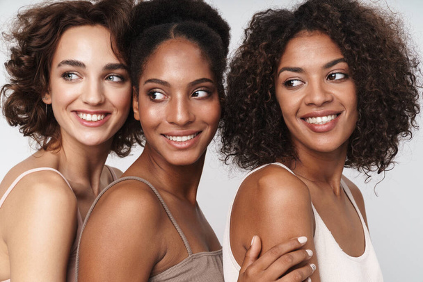 Portrait of three charming multiethnic women smiling and looking aside isolated over white background - Zdjęcie, obraz