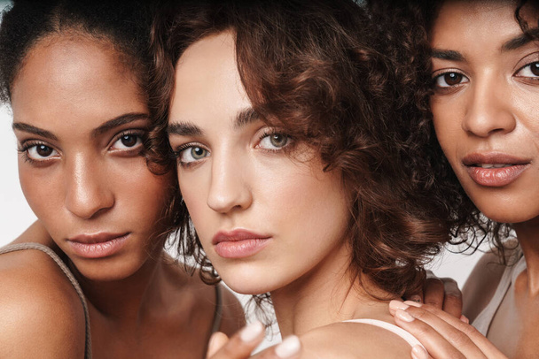 Крупним планом портрет краси трьох привабливих молодих чуттєвих багатоетнічних жінок, які дивляться на камеру ізольовано на білому тлі
 - Фото, зображення
