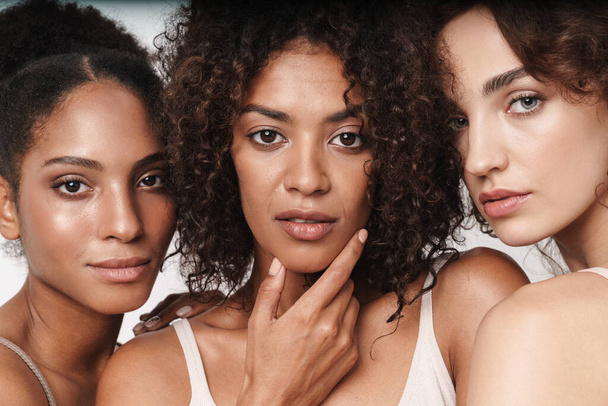 Close up beauty portrait of three attractive young sensual multiethnic women looking at camera isolated over white background - Foto, Imagem