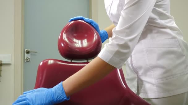 Egy közeli felvétel női fogászati asszisztensről, amint fertőtlenítő oldattal törölgeti az orvosi széket. Sterilizáló orvosi fogászati egység tisztítása a modern fogászati klinikán, orvosi rendelő. 4 k felvétel - Felvétel, videó