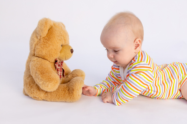 lächelndes kleines Mädchen 6 Monate alt liegt auf einem weißen isolierten Hintergrund in einem hellen Body vor einem weichen Teddybär, Platz für Text - Foto, Bild