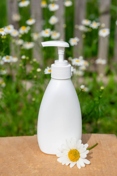 white cosmetic bottle for soap or shampoo on wooden shelf with chamomile background. - Photo, image
