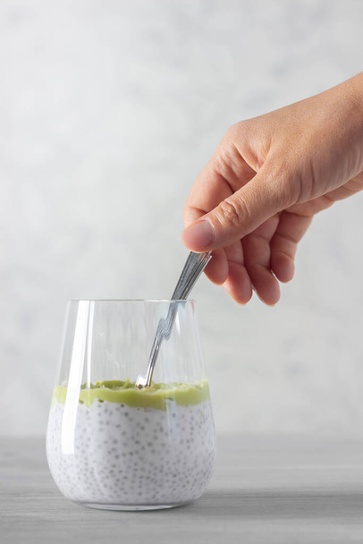 Healthy chia pudding made with avocado and seeds, hand with spoon. White background. - Φωτογραφία, εικόνα