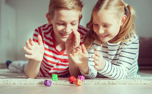Portrait of two cheerful children laying on the floor and playing emotionally with colorful dices - 写真・画像