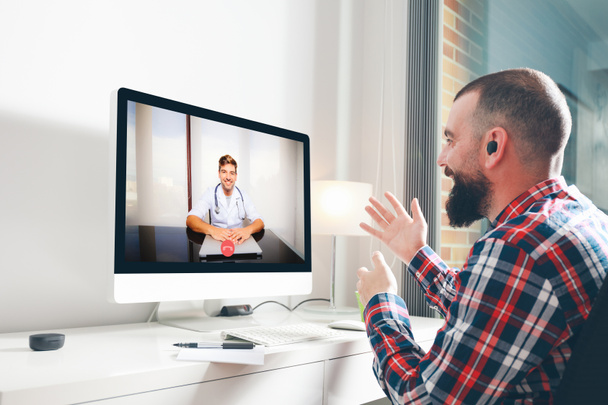 Jovem sentado em frente ao computador conversando com seu médico através de uma videoconferência. Conceito de medicina online - Foto, Imagem