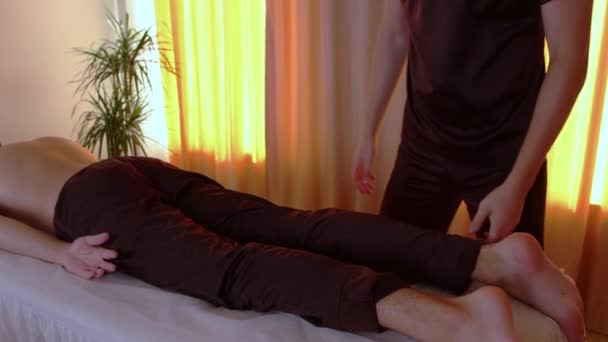 Chiropraktiker-Sitzung im Studio - Arzt beugt seinem Klienten Bein ins Knie - Filmmaterial, Video