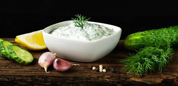 Tzatziki sauce with ingredients cucumber, garlic, dill, lemon on wooden background. Greek cucumber yogurt dip. Banner - Foto, Imagen