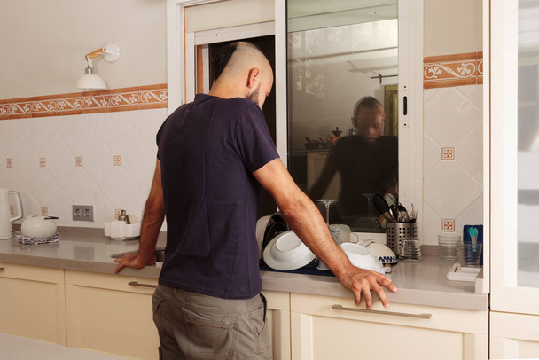 Πίσω όψη ενός νεαρού ισπανόφωνου άντρα που κοιτάζει ένα σωρό πιάτα. - Φωτογραφία, εικόνα
