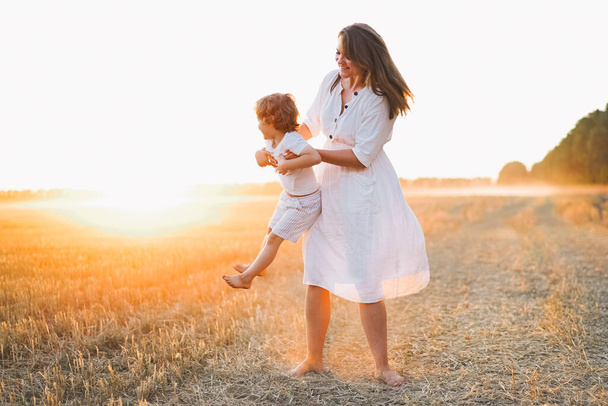 Woman playing with her child on the field during sunset - Photo, Image
