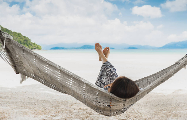 Γυναίκα χαλαρώνοντας στην αιώρα με τα πόδια της επάνω στην τροπική παραλία για καλοκαιρινές διακοπές - Φωτογραφία, εικόνα