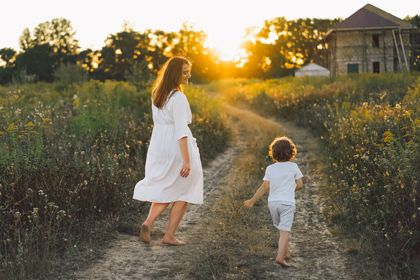vrouw spelen met haar kind op het veld tijdens zonsondergang - Foto, afbeelding