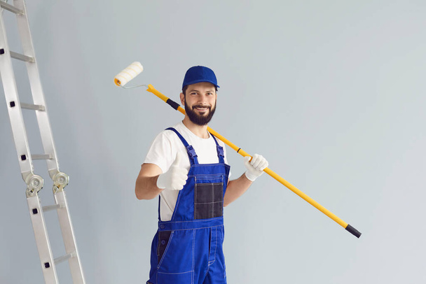 Painter builder worker man smiles with a roller on a grey background. - 写真・画像