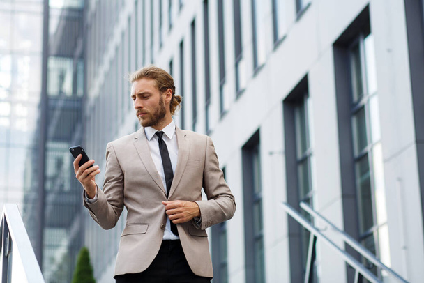 Portrait of a successful young businessman. A curly-haired man in a white shirt with a telephone against the background of a modern business center - 写真・画像