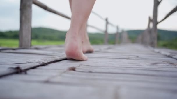 jeune femme pieds nus marche lentement sur un pont en bois, calme mouvement paisible, montagne et arbres sur le fond, sortir de la boîte, détente dans la nature liberté, caméra basse angle - Séquence, vidéo