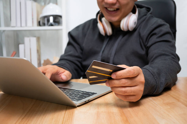 Ein Mann hält eine gefälschte Kreditkarte in der Hand und bezahlt online mit einem Laptop, nachdem er Produkte über das Internet bestellt hat. Das Konzept der Technologie für den E-Commerce (elektronischer Handel)) - Foto, Bild
